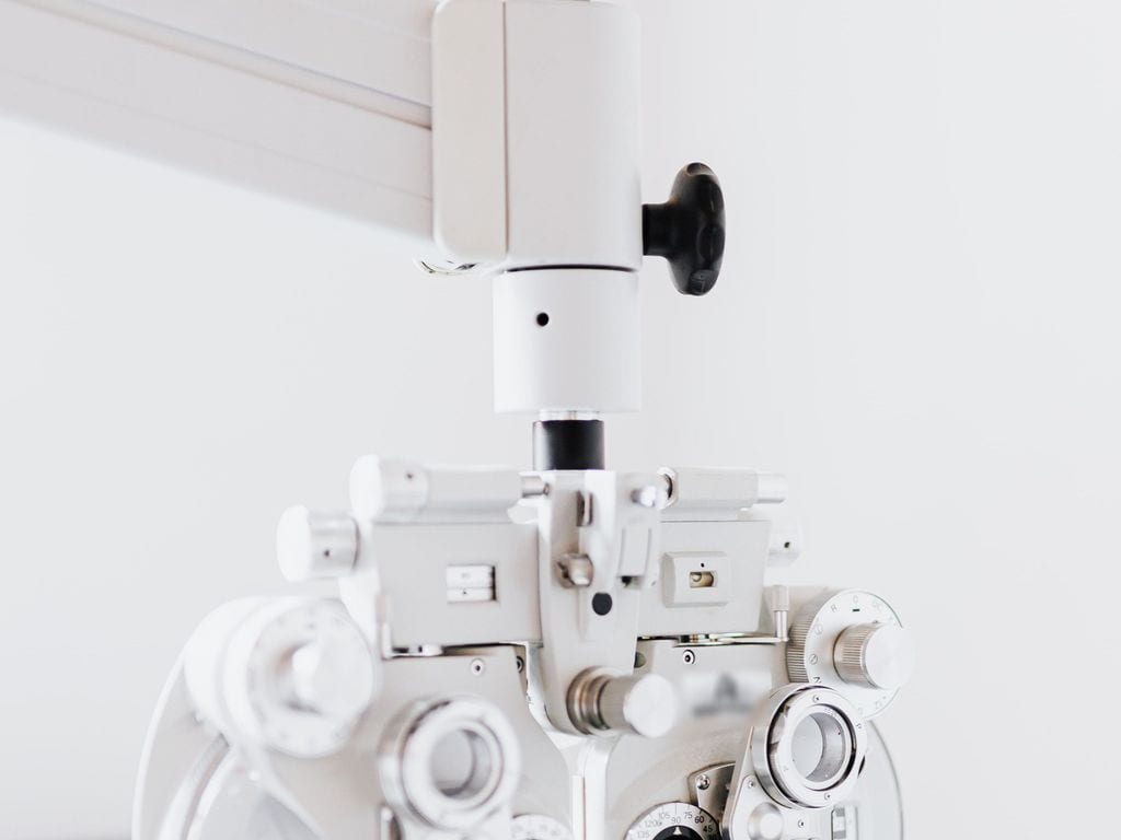 A white phoropter in an ophthalmology office, against a light wall.